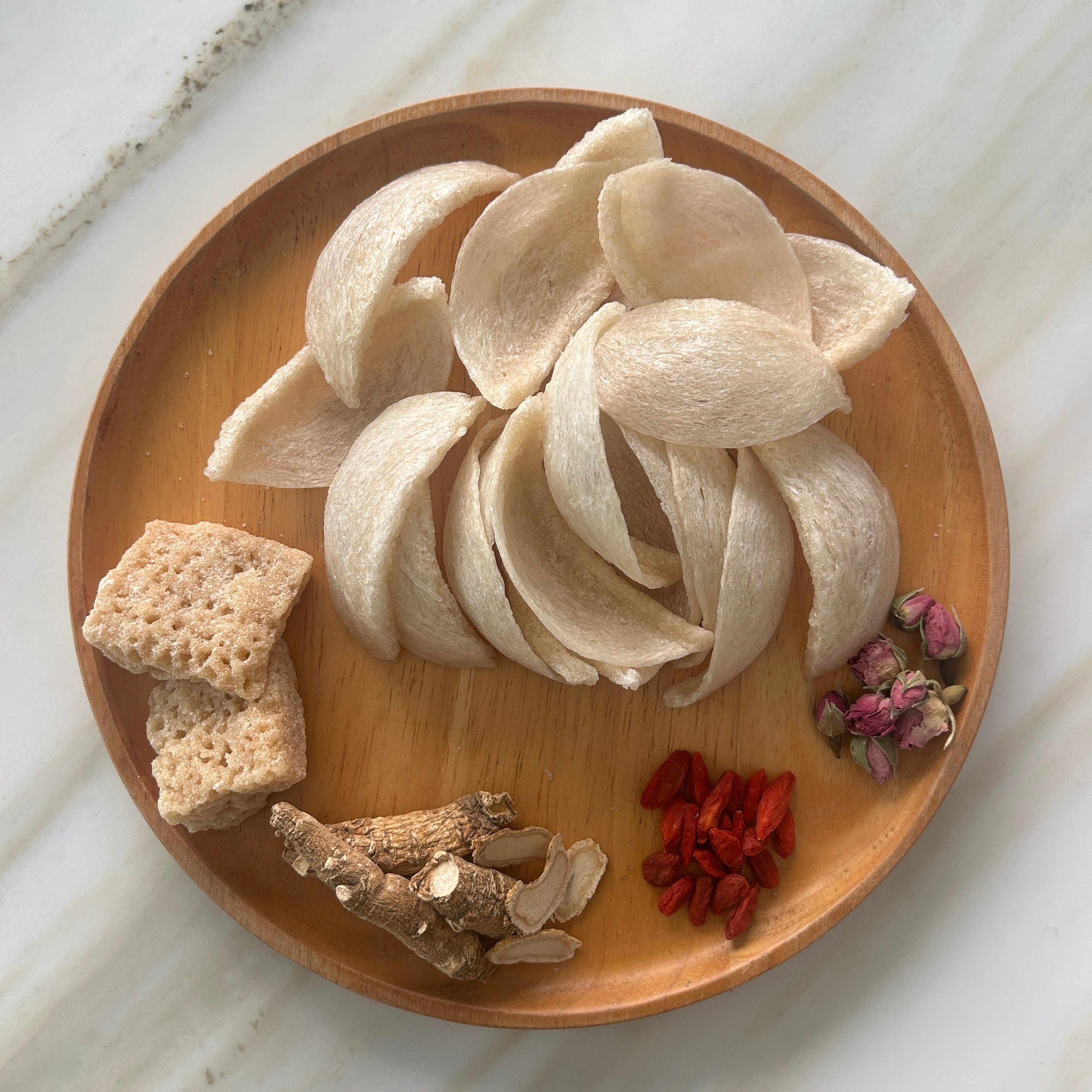 Wooden plate with premium dried bird's nest, goji berries, and dried ginseng roots on a marble surface.
